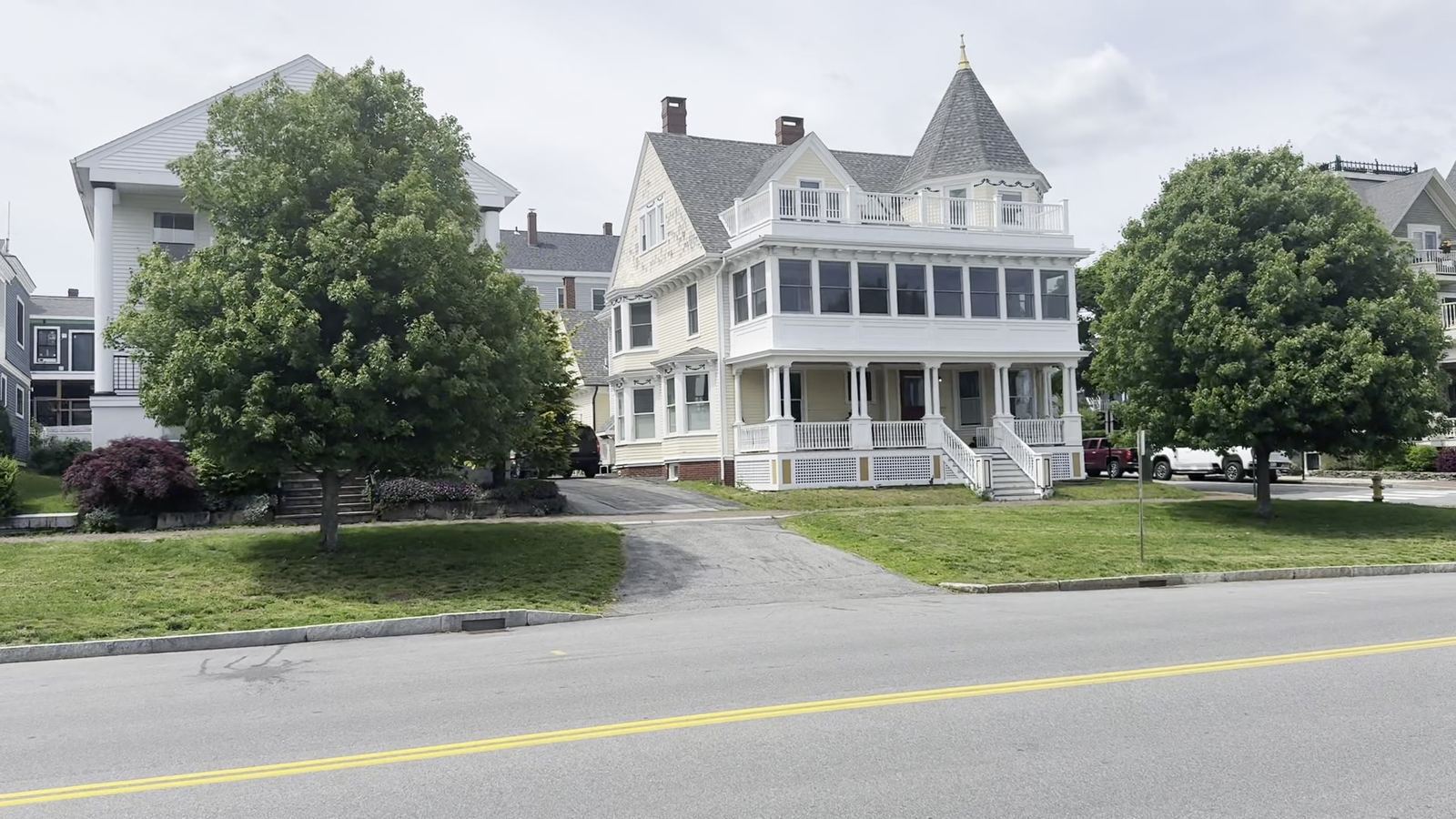 A white Victorian house with a wraparound porch on a residential street in Portland, Maine